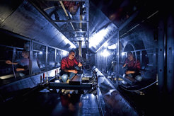 A room with dark metal walls and intricate reflections that catch the light, with scientist Eberhard Bodenschatz, a man in his early 60s in a red shirt, working at a table.